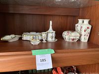 Front view of assorted porcelain decorative glassware including vases, decanter, ashtrays, and small dishes with floral designs and gold trim.