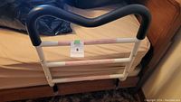 Front view of bedrail safety support rail mounted on a bed, showing black padded top handle and white metal frame.