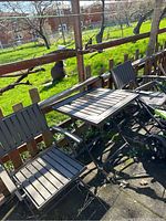 Three-piece outdoor bistro set of two chairs and one table positioned near a wooden fence in a garden setting.