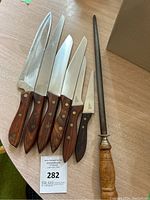 Full view of the six Japanese-style knives with wooden handles and sharpening steel rod on a table.