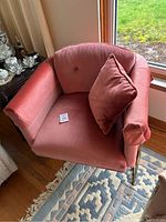 Front angle view of coral pink velvet armchair showing tufted back cushion and matching pillow on seat.