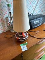 Front view of one MCM ceramic lamp showing brown and red glaze base with off-white shade, placed on wood surface near stereo.