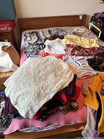 Full bed view showing wooden headboard and mattress with clothes piled on top