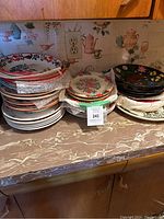 Wide image showing multiple stacked plates and bowls with floral hand painted designs on a countertop.