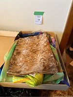 Box containing multiple folded scarves in various colors and patterns, primarily showing brown abstract printed scarf on top