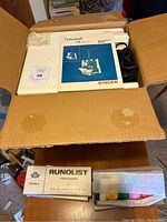 Cardboard box with foam inserts, Singer manual on top, power cord at right, partial view of thread boxes below