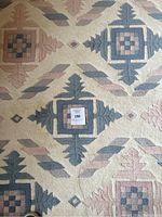 Top-down photo showing the diamond and leaf geometric pattern in blue and pink on cream wool rug.