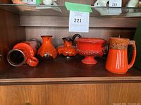 Shelf display of five vintage fat lava style pottery pieces in bright orange and red with textured glazes.