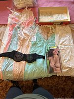 Overview of vintage lingerie items including nightgowns in pastel colors, black strapless bra, cream lace slip, and two boxed Warner's bras