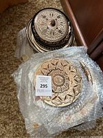 Stack of various sized copper plates with engraved floral and leaf designs, wrapped in bubble wrap.