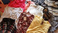 Multiple women's tops of various colors and patterns laid out on a bed showing tags on some items and a variety of sizes including large and XL.