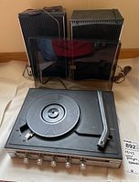 Front view of the turntable with speakers and dust cover taken off and cords visible.