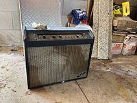 Full view of Regal guitar amplifier placed on concrete garage floor, showing overall black enclosure and front mesh panel with the Regal logo.