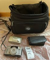 All contents laid out: Canon camera, Olympus camera, large black bag, small black case, ID card