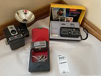 Kodak Instamatic 44 camera gift set with camera in foam insert inside original yellow box, visible instruction manuals, Kodak Brownie Hawkeye camera with large flash reflector and gear case, and Sunbeam two-head electric shaver with cord and red case.