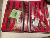 Photo showing multiple knives in protective red case with black handles and gold lettering 'Castle', new in package.