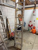 Full view of the metal extension ladder showing the rungs, side rails, and the yellow extension rope in a garage setting with holiday decorations visible in background.