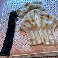 Photo showing the fur stole, collar, and various fur remnants displayed on a bed covered with a peach-colored quilted cover.