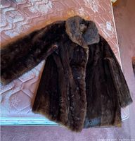 Full view of the brown fur coat spread out on a mattress showing overall condition and length.