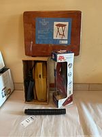 Lot contents including sealed Select Edition folding table, Bonaire yellow hand vacuum in box, Dirt Devil 0889X hand vacuum in original box, and a black vacuum hose attachment.