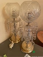 Two glass table lamps with glass globe shades, prism accents, and metallic bases shown with cords coiled.