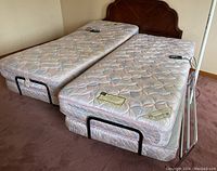 Photo showing two separate adjustable 40x80 mattress sections with wired handheld controls on top, placed side by side on carpet. Metal frames with wheels and different height support visible.