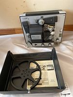 Full view of Bell and Howell 8mm film projector with take-up reel and front cover laid out, showing projector in upright position.