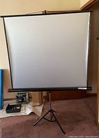 Full view of the projector screen standing upright, showing the white projection surface and tripod base.