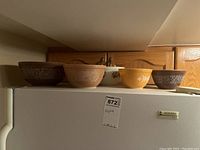 Five vintage Pyrex bowls displayed in a row on top of a refrigerator, showing various colors and floral patterns.