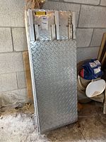 Side and front view of folded metal ramp showing the diamond plate surface and handle.