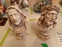 Pair of cream-colored porcelain religious busts, one male with crown of thorns, one veiled female, on ornate bases
