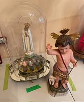 Virgin Mary figurine under clear glass dome with mirrored base and small kneeling figures surrounding the base of the statue.
