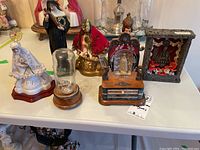 Seven religious figurines in different styles and sizes arranged on a glass table.