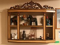 Wooden two tier wall shelf with ornate carved top, gold accents. Shows layout with various small figures including horses, flower, rooster.