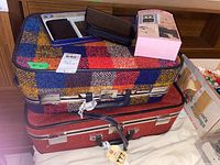 Photo showing three suitcases stacked, with various small items on top including a mini screwdriver set, black case, and a box likely for the radio.