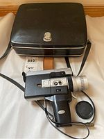 Canon Auto Zoom 518 Super 8 camera shown with black hard shell carrying case, camera lens cap beside it.