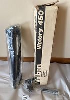 Velbon Victory 450 tripod collapsed and wrapped in original plastic next to its box and separate mount also wrapped in plastic.