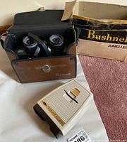 Bushnell binoculars model 13-8465 inside a brown leather carrying case, with the original Bushnell cardboard box in the background.