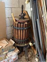 Wine press stored in garage corner, showing full view of wood and metal construction with base and screw press handle.