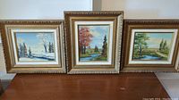 Three framed oil paintings by O.J. Coghlin displayed side by side on a table.