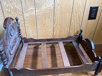 Full view of dolls bed showing the carved headboard, side rails, and slatted base.