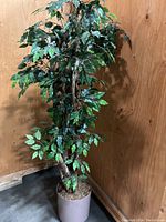 Full view of large artificial tree showing foliage, branches, and base pot against wood wall background.