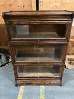 Front view of entire bookcase showing three glass-fronted sections with drop-front doors and brass knobs