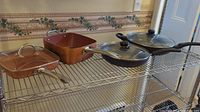 Three square Copper Chef pans and two round frying pans with lids on a metal shelving rack.