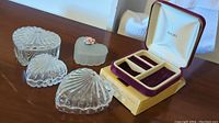 Four heart-shaped glass trinket boxes (three clear patterned, one frosted with pink flower and chip) and vintage Avon jewelry case with original box.