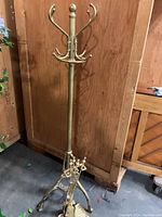 Full view of brass coat rack with brass fireplace tools gathered at base, showing overall structure and design.