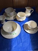 Photo showing full set of three tea cups with saucers, egg holder, sugar and creamer with yellow ribbon detail on blue cloth background.