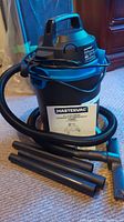 Mastervac vacuum cleaner with hose and extension wands shown assembled on a carpeted floor.