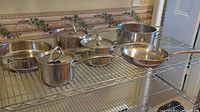 Set of 6 stainless steel pots and pans with lids and steamer basket arranged on metal rack