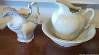 Two pitchers displayed together: a white ironstone pitcher with matching basin and a blue and white decorative pitcher.